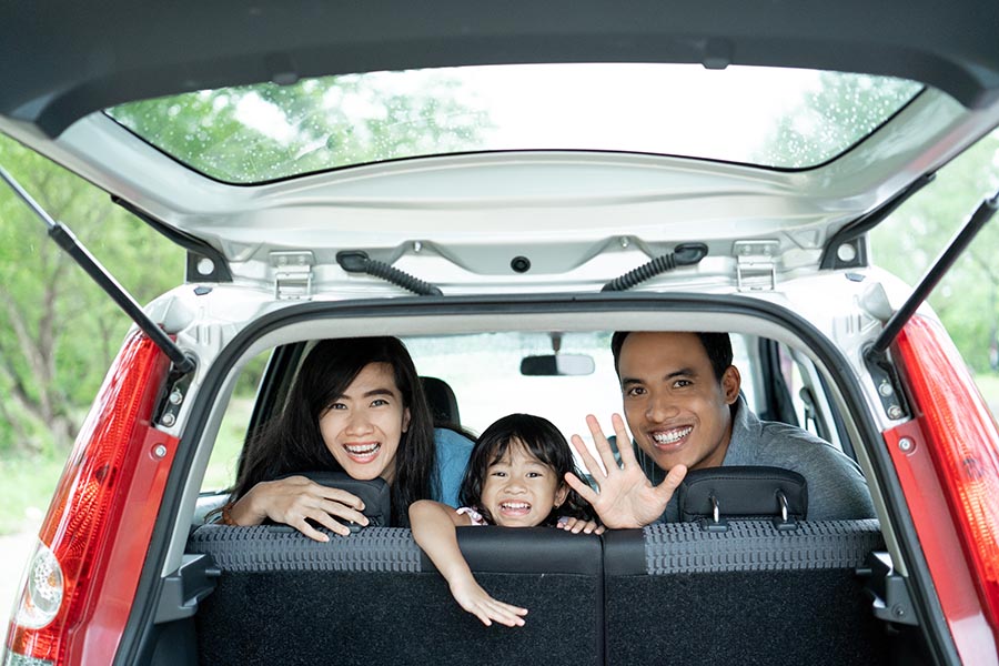 Client Center - Family Peeking Out the Back of Their Hatchback Car on a Sunny Tree-Lined Street